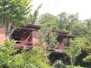 A two-story brick building with a balcony, surrounded by lush greenery. - Pousada Colina Verde (Garopaba)