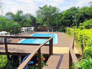 A wooden deck with a pool, surrounded by greenery and a wooden fence. - Pousada Colina Verde (Garopaba)