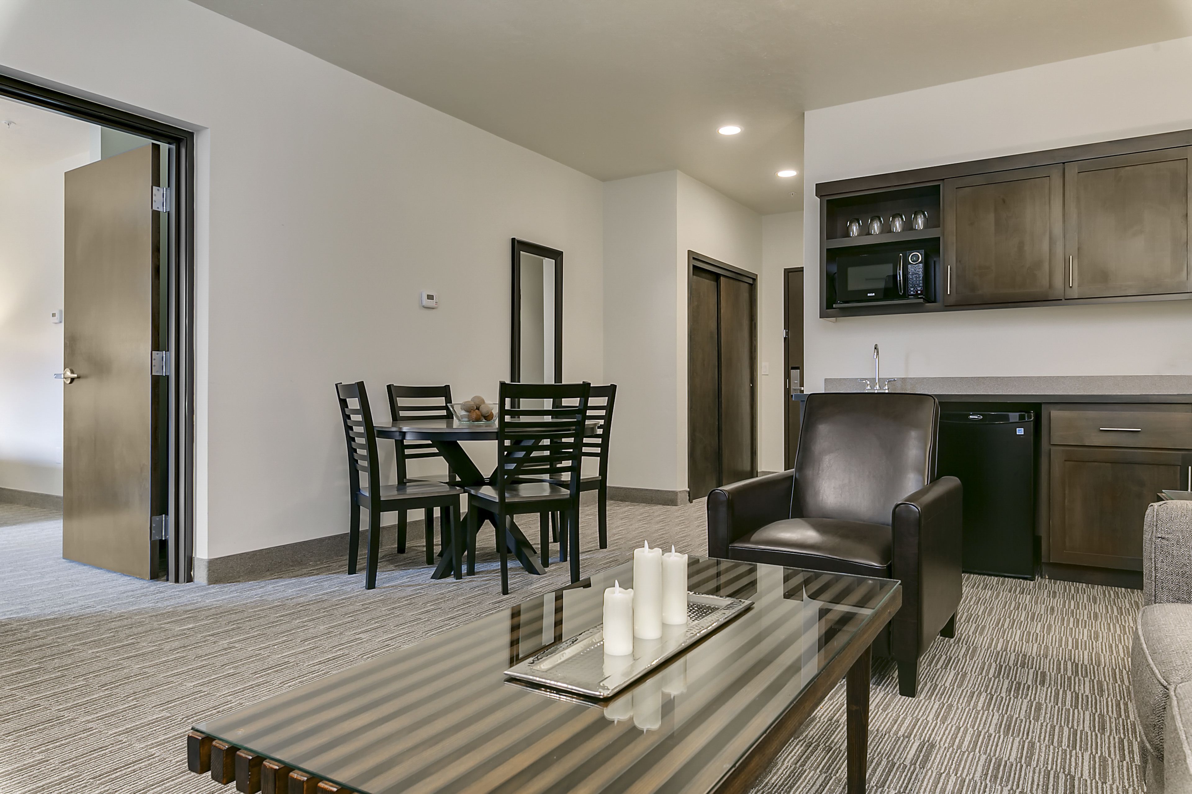 A modern hotel room with a dining area, a kitchen, and a seating area.