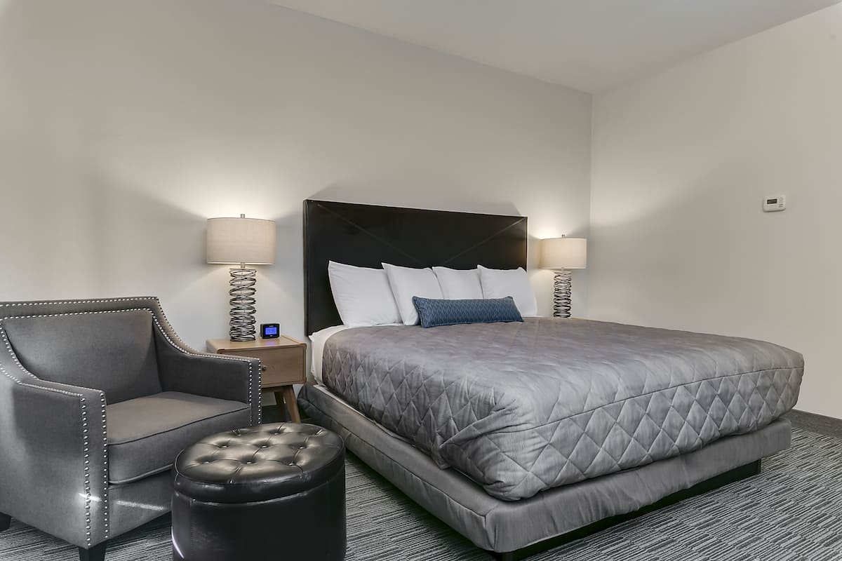 A hotel room with a large bed, a chair, a small table, and two lamps.