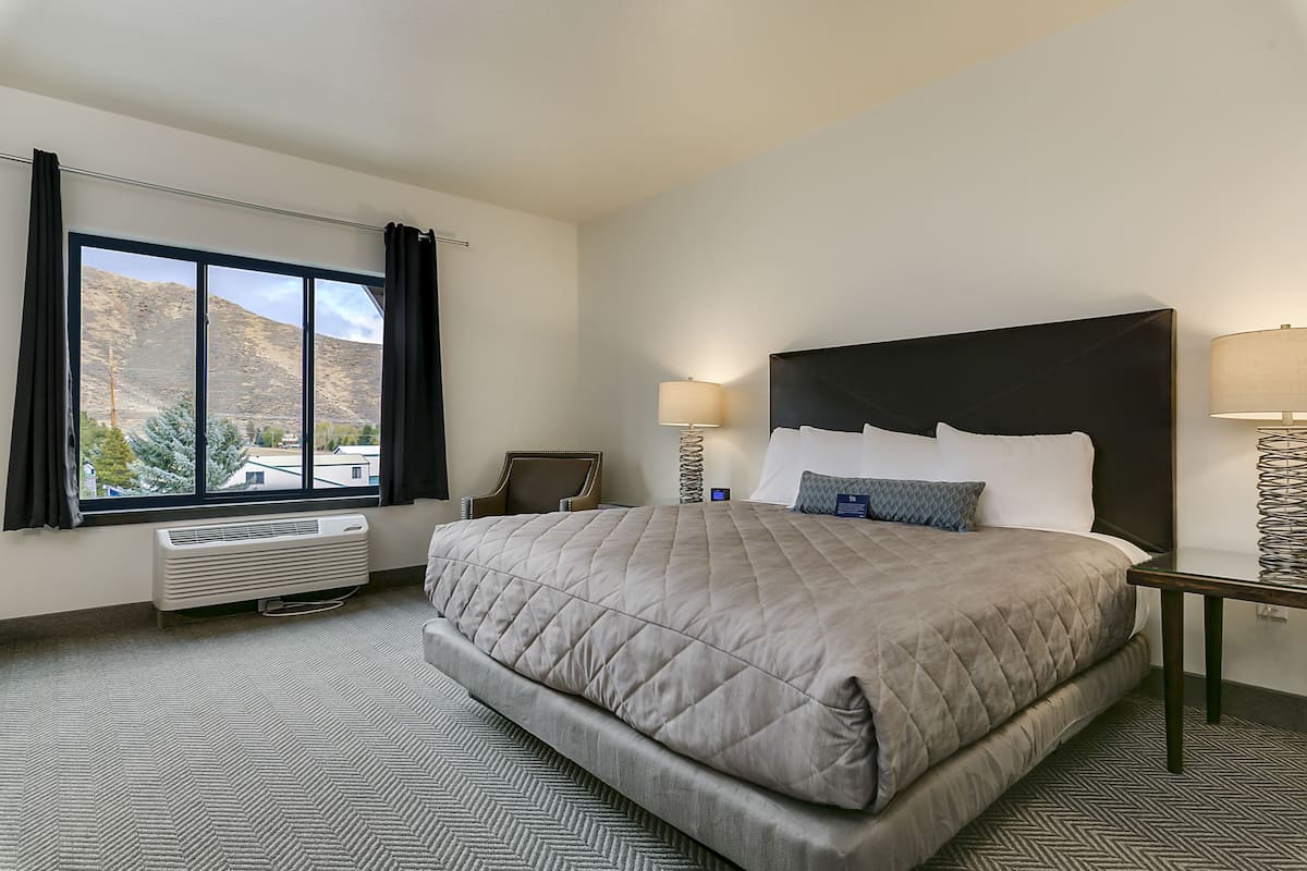 A hotel room with a large bed, a view of mountains, a desk, and a chair.
