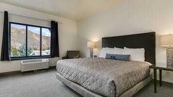 Een hotelkamer met een groot bed, uitzicht op bergen, een bureau en een stoel.