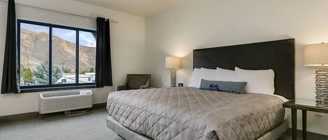 A hotel room with a large bed, a view of mountains, a desk, and a chair.