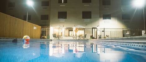 Una piscina con un flotador salvavidas, una zona de estar techada y un edificio con varias ventanas al fondo.