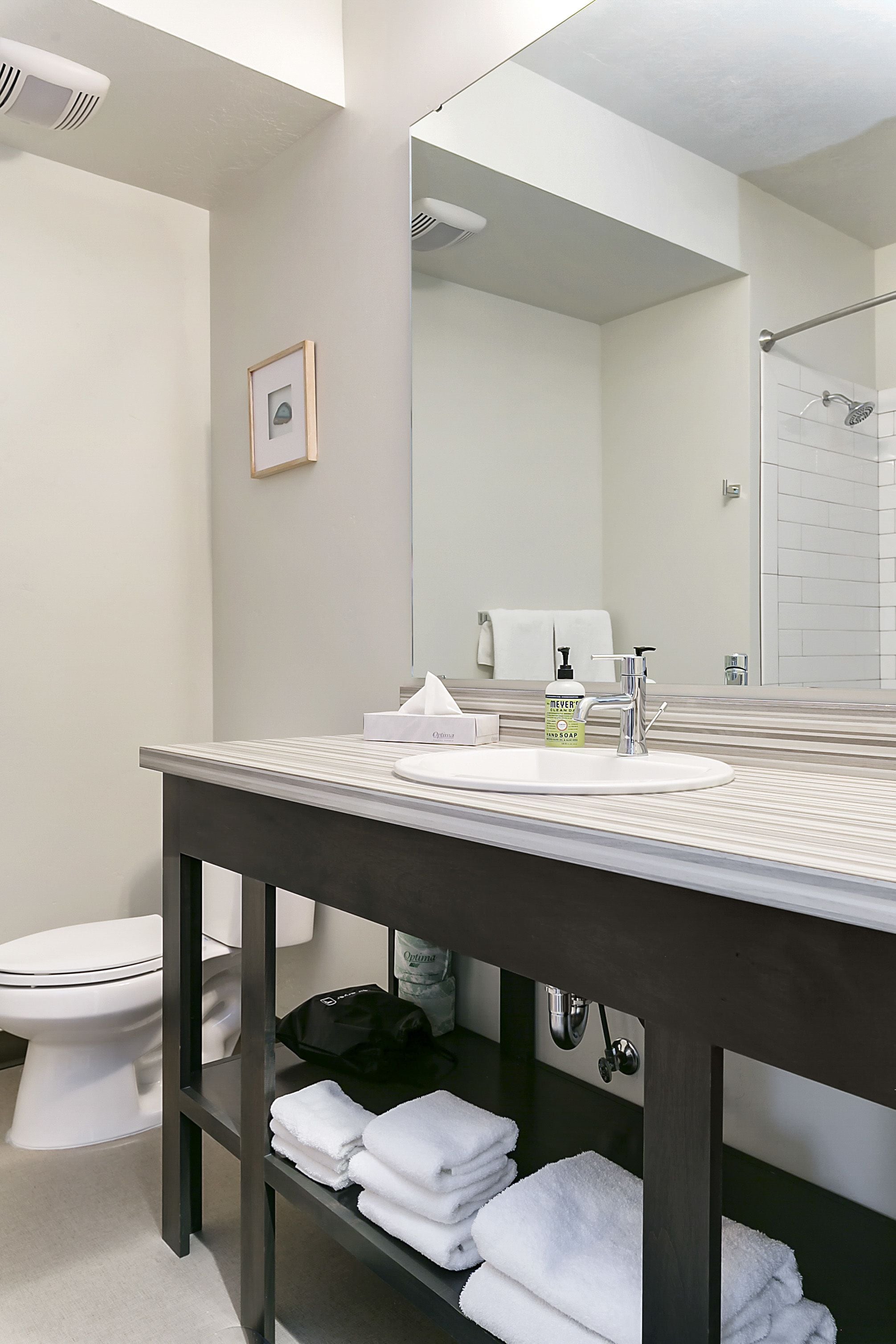 A modern bathroom with a large mirror, a white sink, and a dark wooden vanity.