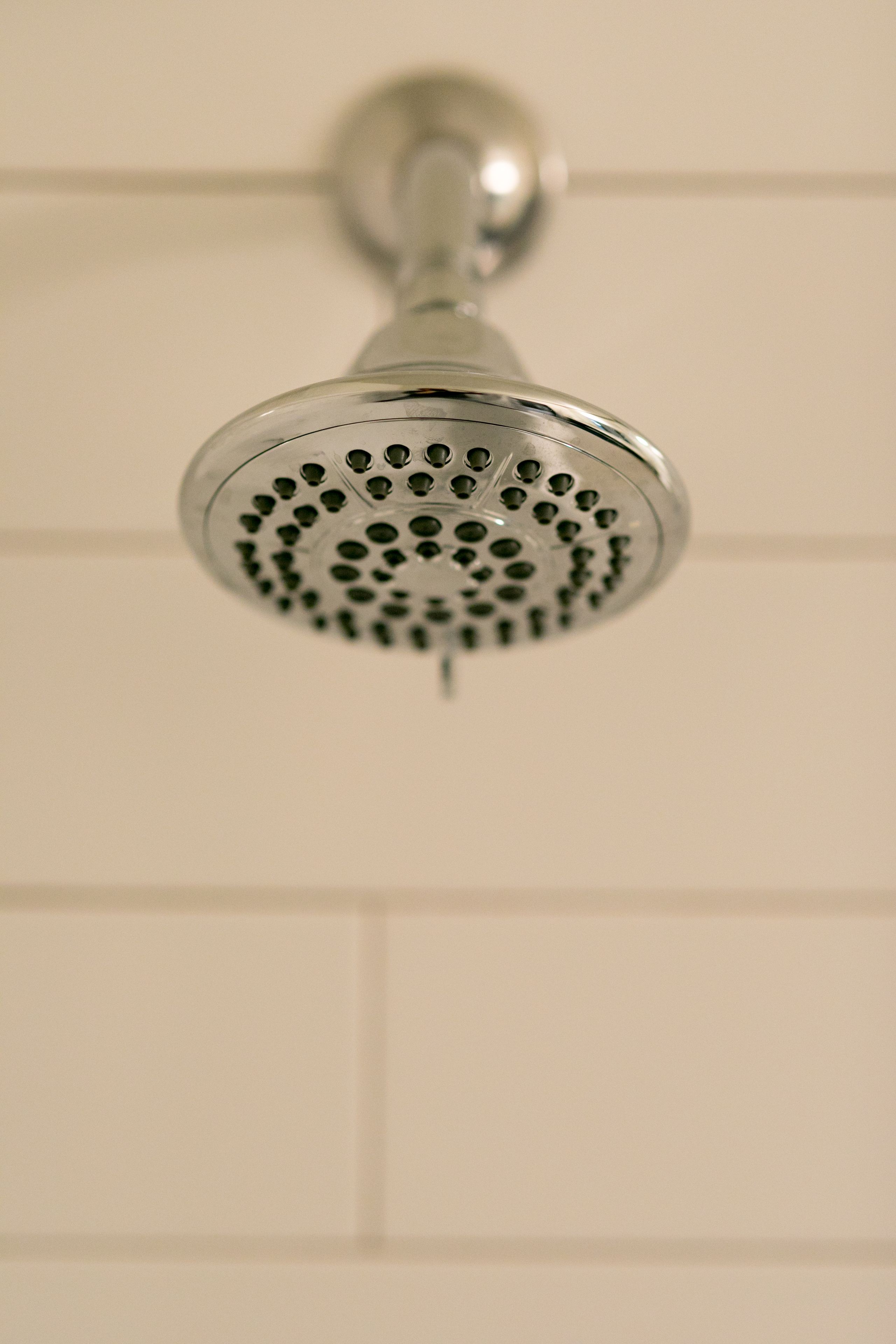 A showerhead with a round, perforated design, mounted on a wall with a grid pattern.