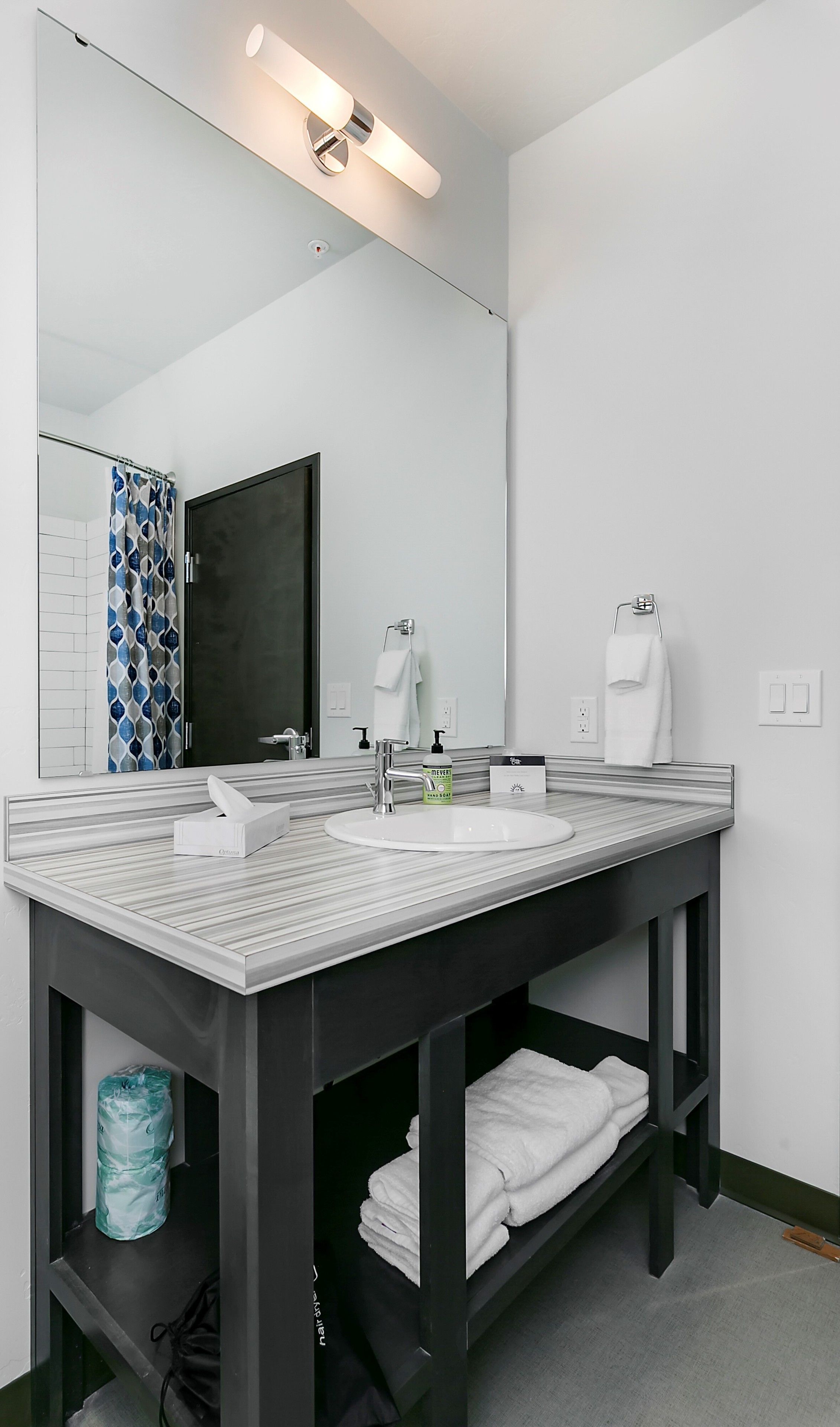 A modern bathroom with a large mirror, two sinks, and a vanity with a towel rack.