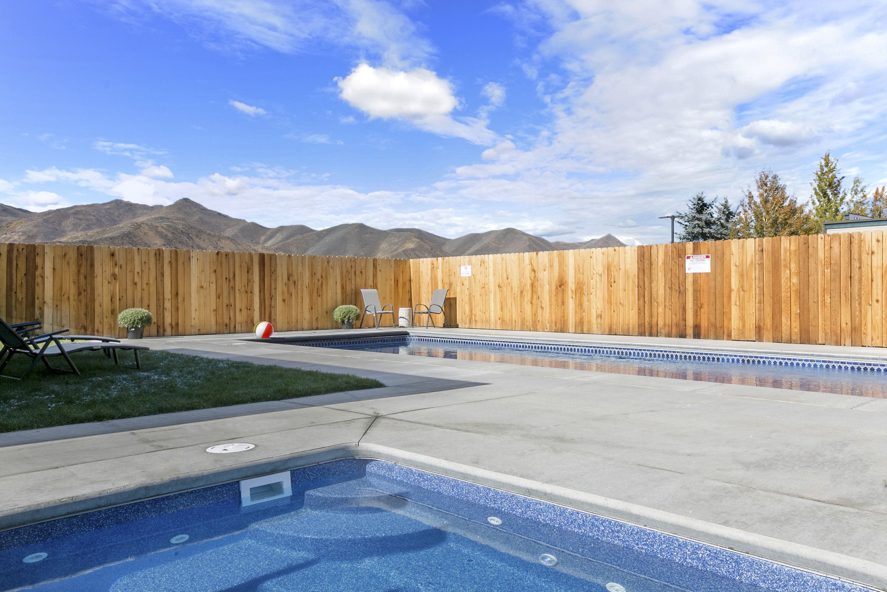 A backyard with a swimming pool, wooden fence, and mountains in the background.