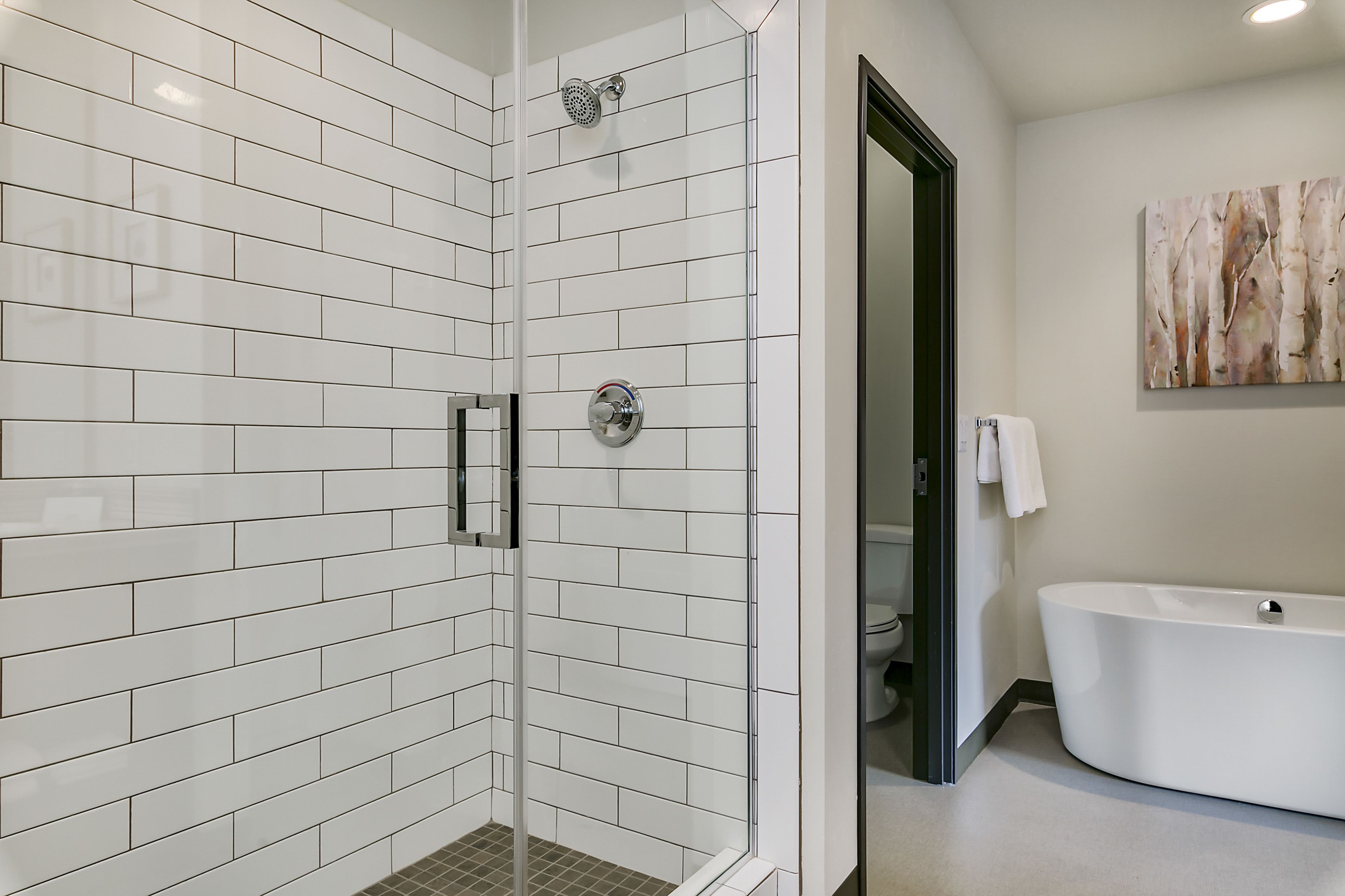A modern bathroom with white subway tiles, a glass-enclosed shower, a freestanding bathtub, and a minimalist design.