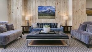 Een moderne woonkamer met een blauwe bank, twee bijzettafels met lampen, een salontafel met een plant, en een groot schilderij van een berglandschap aan de muur.