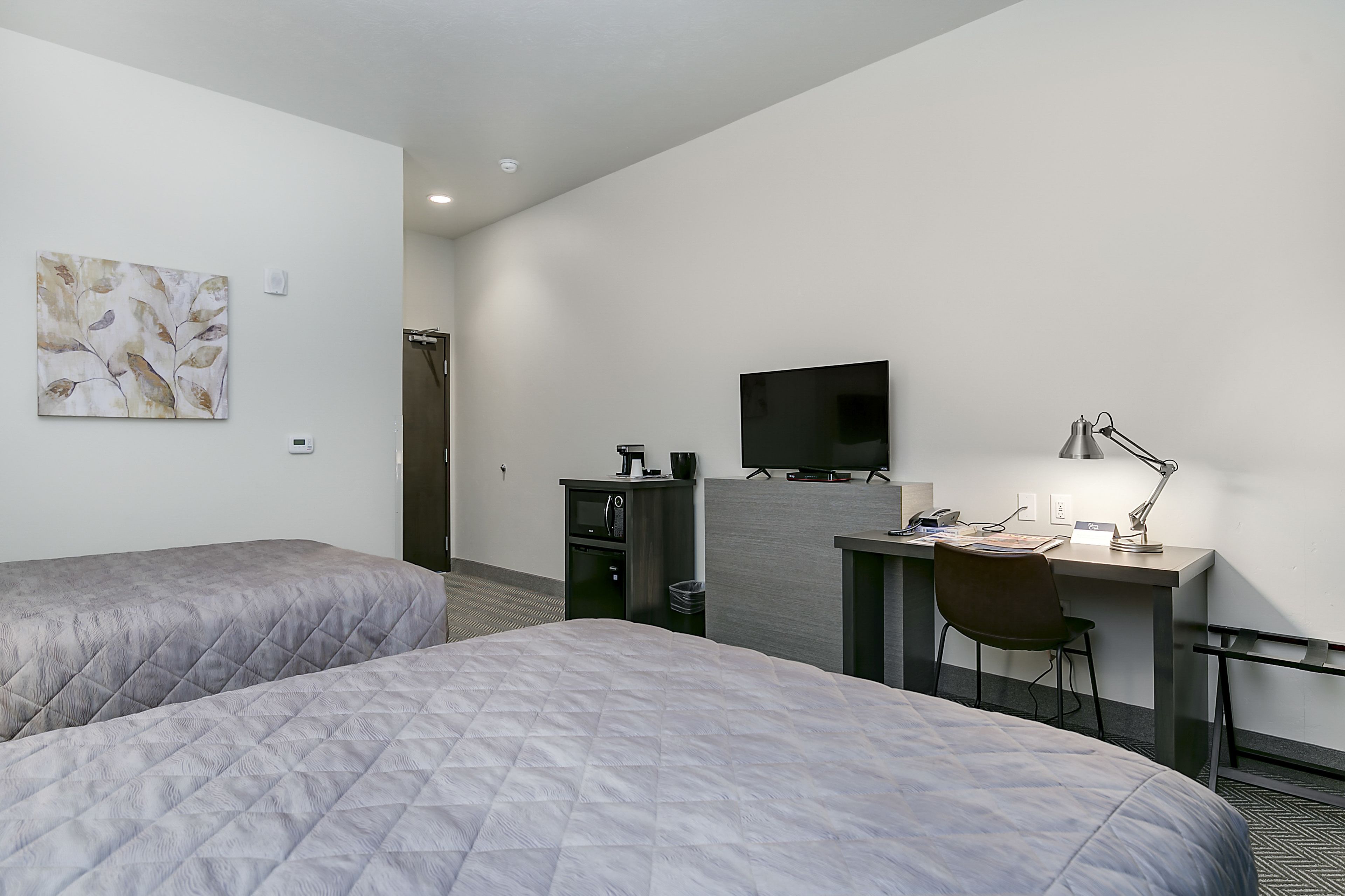 Une chambre d’hôtel avec deux lits, un bureau avec une chaise, une télévision et une petite kitchenette.