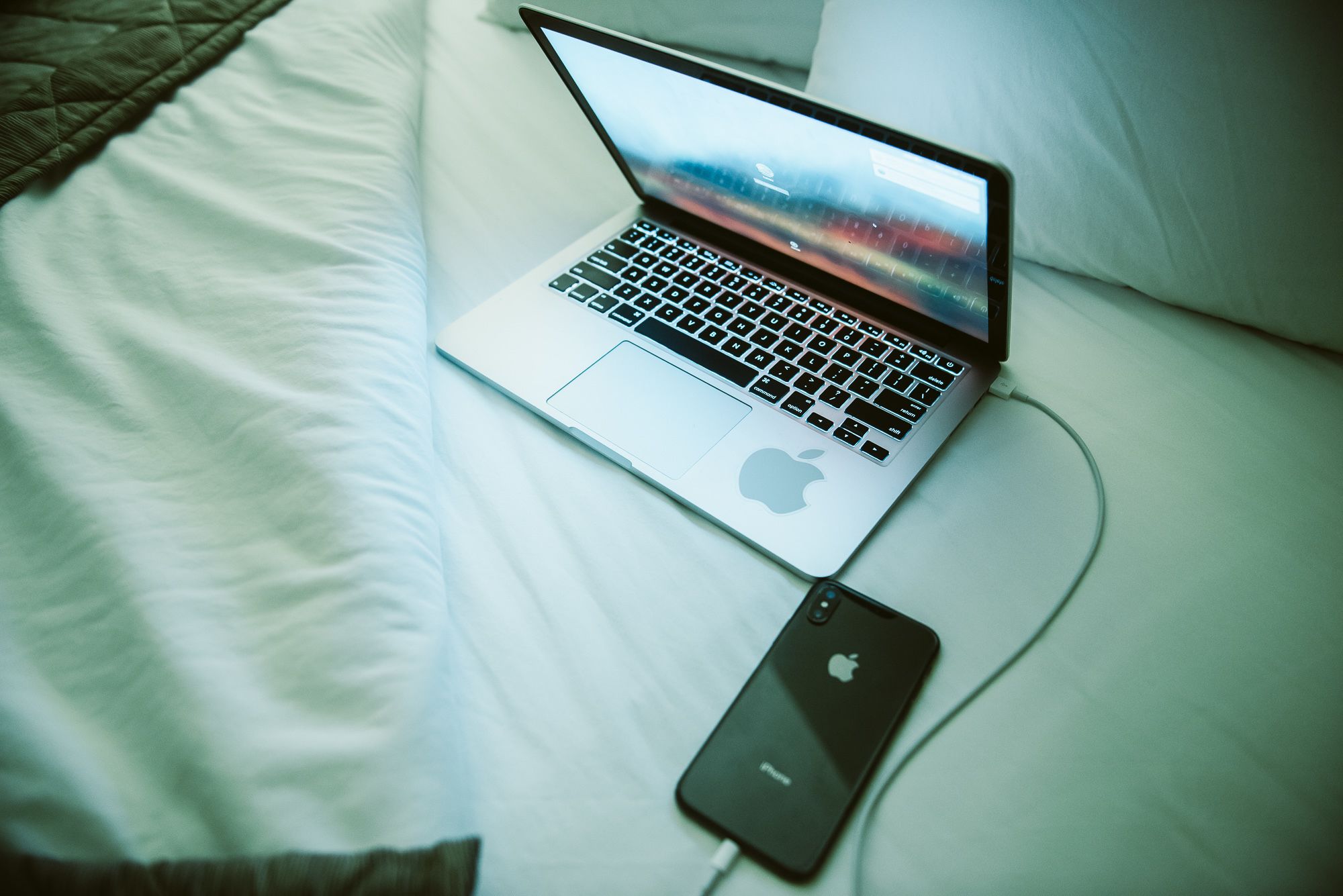 A laptop on a bed with a smartphone connected to it.