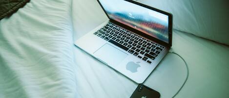 A laptop on a bed with a smartphone connected to it.