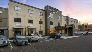 Een hotel met een modern design, met een parkeerplaats met meerdere auto's en een heldere lucht.