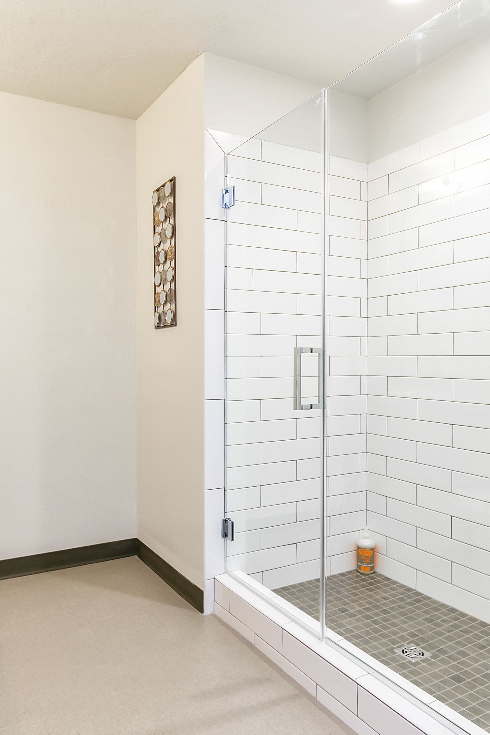A corner shower with white subway tiles, a glass door, and a small bottle on the floor.