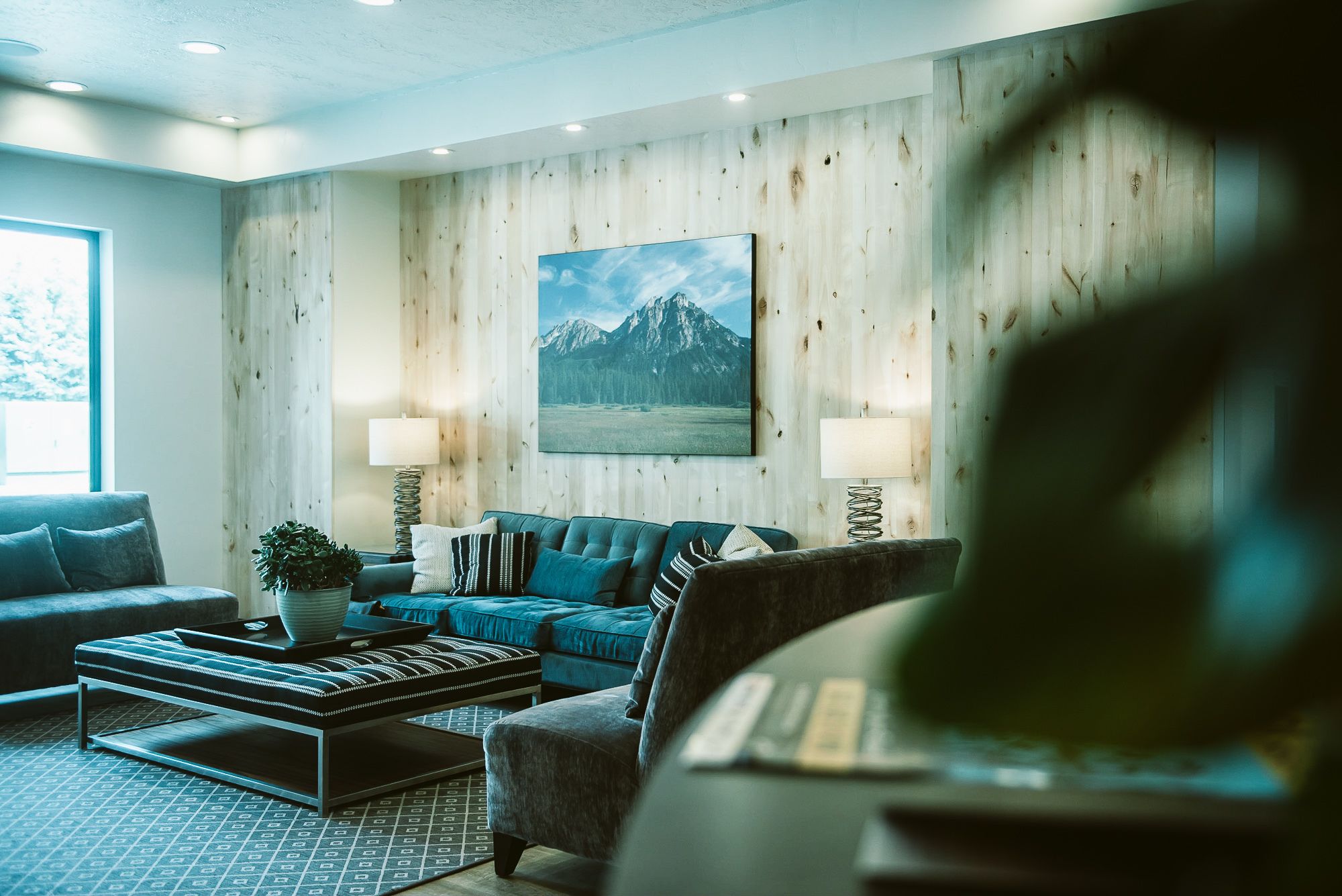 A modern living room with a wooden wall, a mountain painting, and a blue sofa.