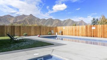 Un jardin avec une piscine, une clôture en bois et une vue sur les montagnes.