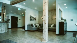 Een ruime lobby met een houten receptiebalie, twee banken, een grote houten zuil en een lijst met een afbeelding aan de muur.