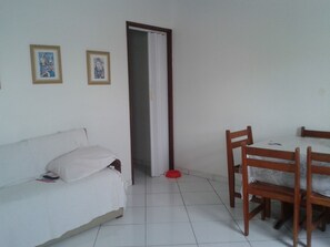 A room with a white sofa, a dining table with chairs, and two framed artworks on the wall.