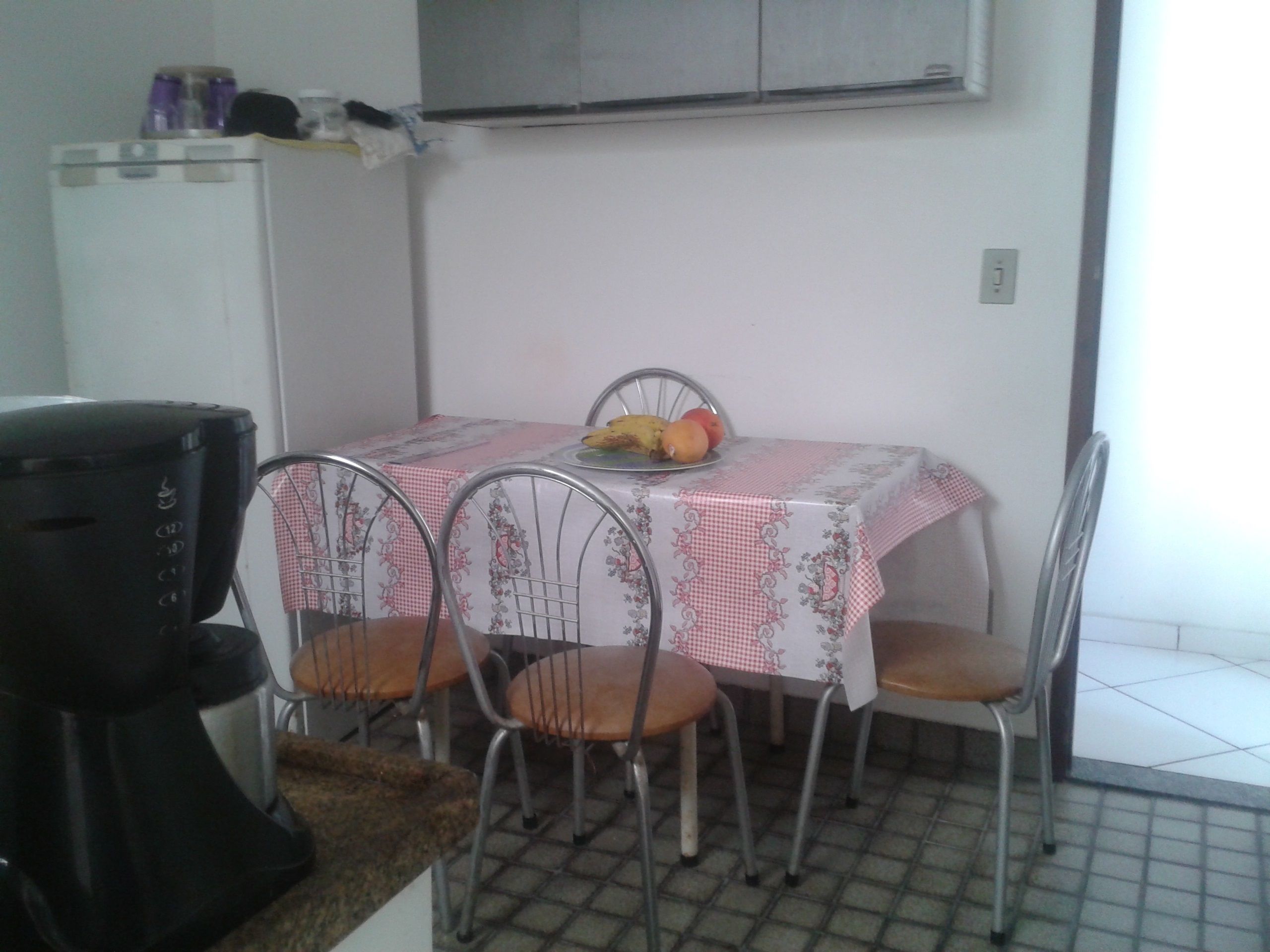 A small dining area with a table covered by a checkered tablecloth, four metal chairs, and a fruit plate on the table.