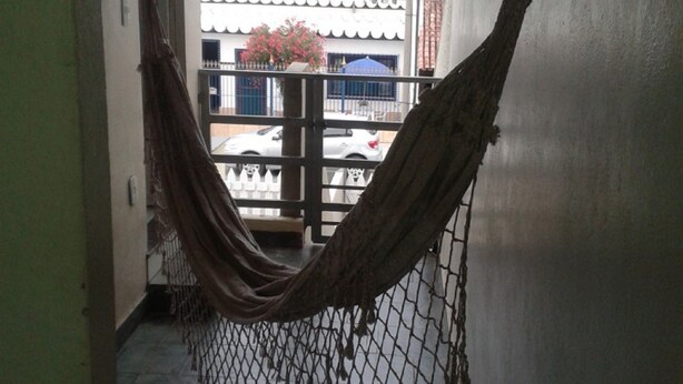 A hammock in a hallway with a view of a balcony and buildings outside. - Férias na Beira da Praia em Cabo Frio (Cabo Frio)