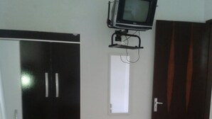 A bedroom with a bed, a wardrobe, a television mounted on the wall, and a door with curtains. - Férias na Beira da Praia em Cabo Frio (Cabo Frio)