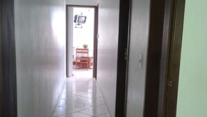 A narrow hallway with white tiled flooring leading to a room with a bed and a window. - Férias na Beira da Praia em Cabo Frio (Cabo Frio)