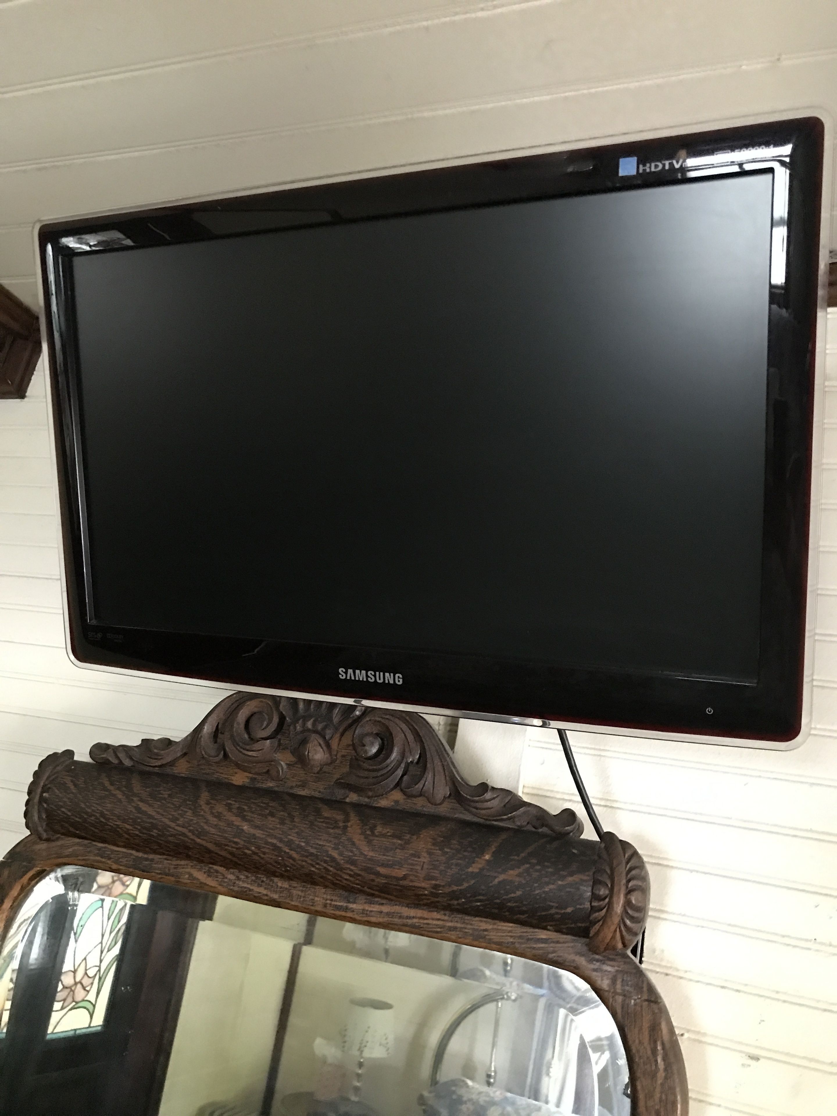 A Samsung TV mounted on a wooden stand with a mirror below it.