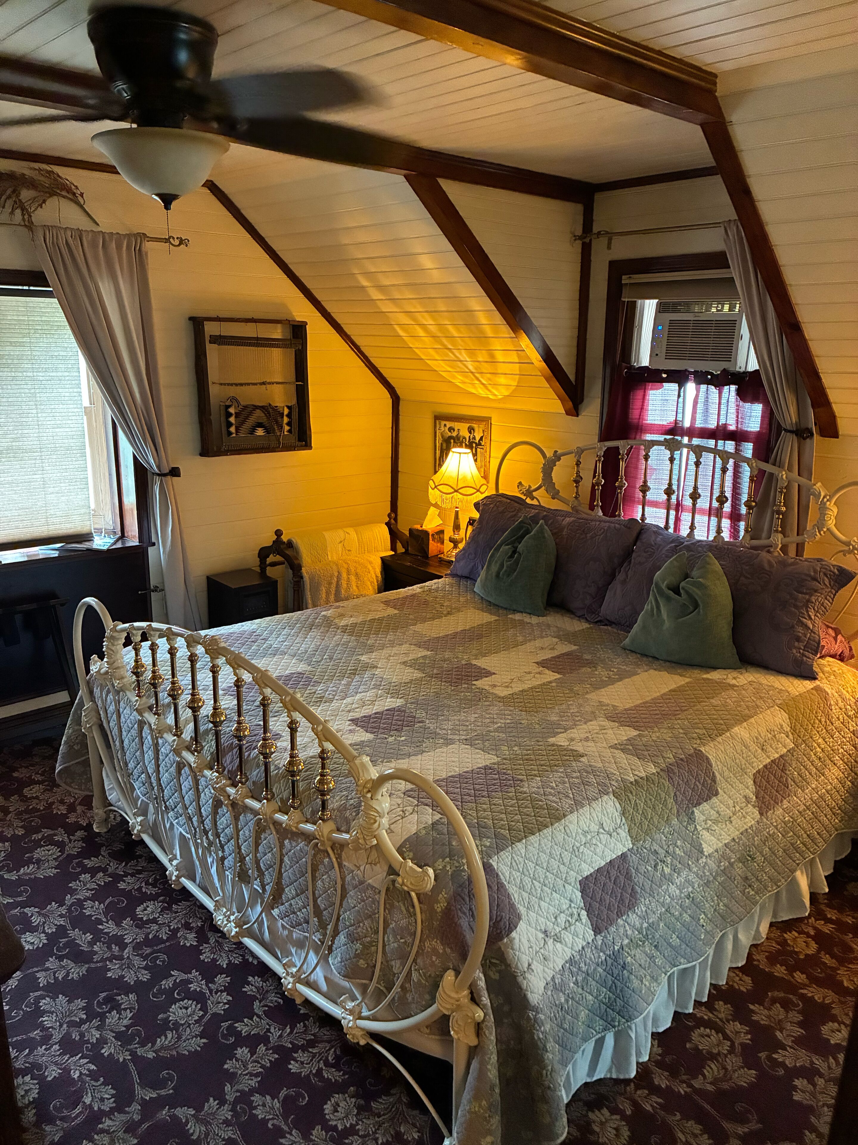 A bedroom with a bed, a nightstand, a lamp, a ceiling fan, and a window with curtains.