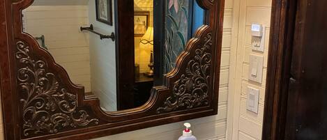 Un baño con un espejo ornamentado, un lavabo negro y dos luces fijadas a la pared.