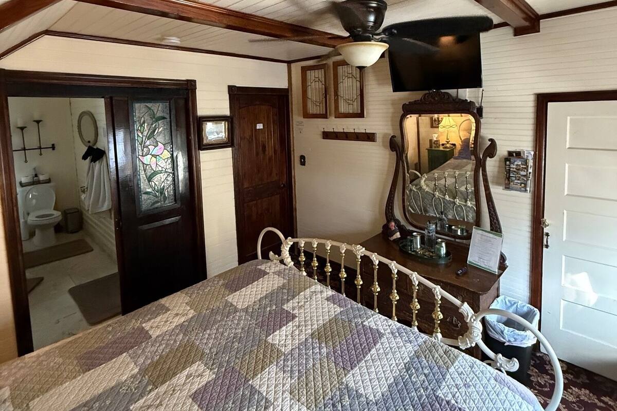 Un dormitorio con techo de madera, una cama con colcha, un aparador, un espejo y una puerta que da a un baño.