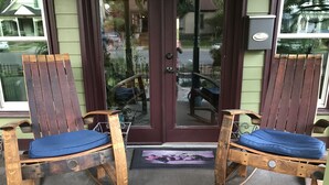 Two wooden rocking chairs with blue cushions on a porch with a glass door and a doormat.