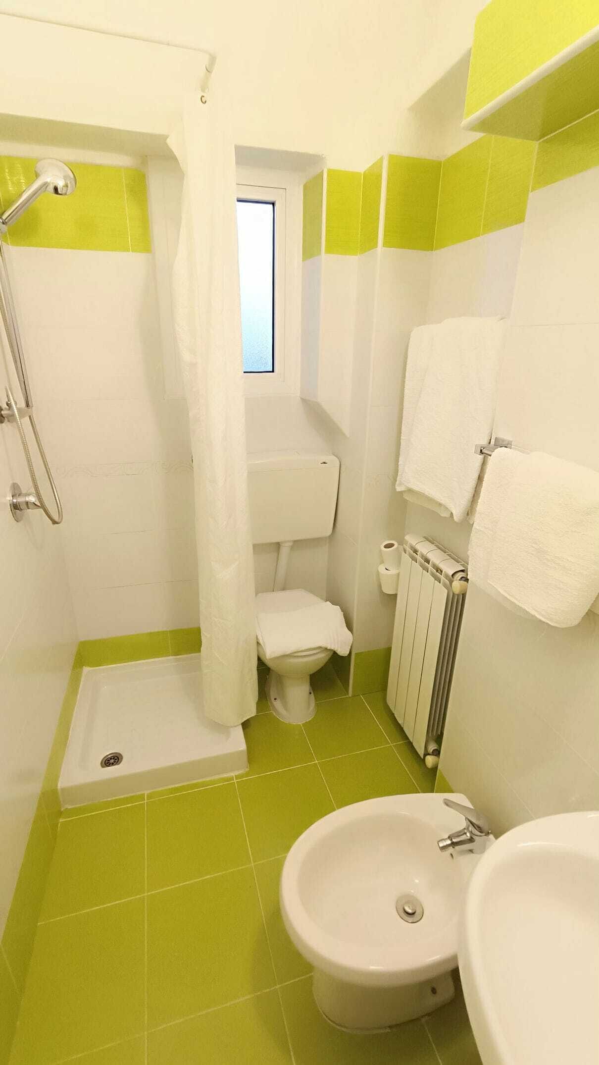 A bathroom with a shower, toilet, sink, and a window.