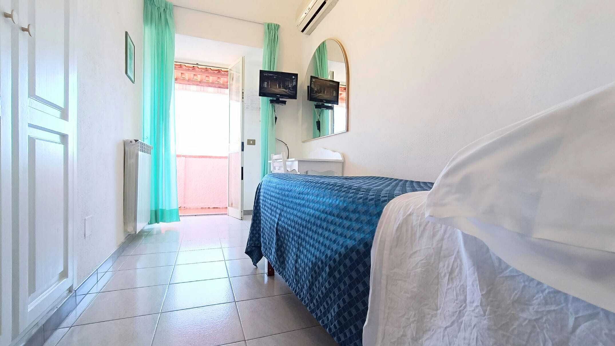 A hotel room with a bed, a desk, a chair, a TV, and a bathroom.