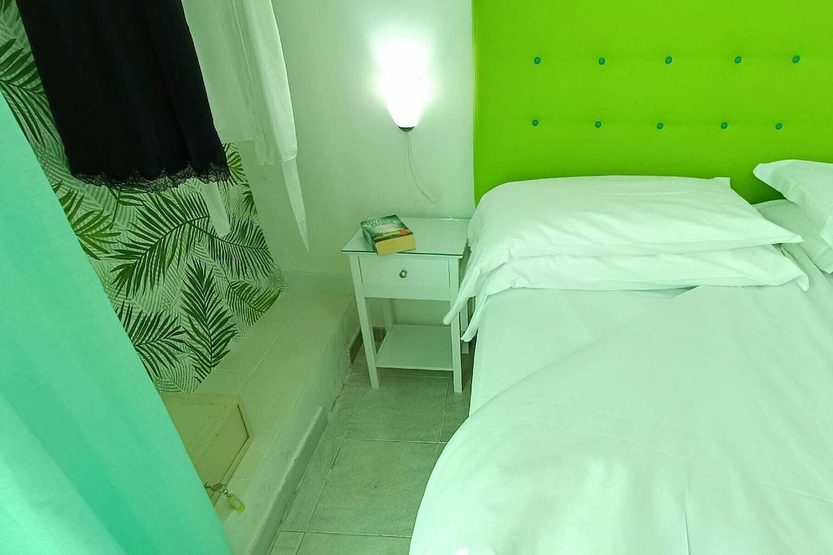 Een kamer met twee bedden, een nachtkastje, een wandlamp en een kamerbedekking met een patroon.