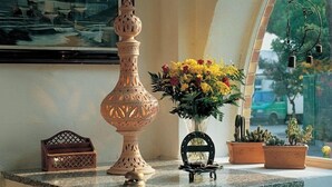Een tafel met een marmeren blad, een decoratieve vaas, een klein houten doosje, een metalen bel, een metalen frame en potplanten.