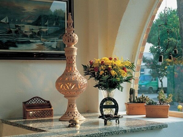 A marble-topped table with a decorative vase, a small wooden box, a metal bell, a metal frame, and potted plants.