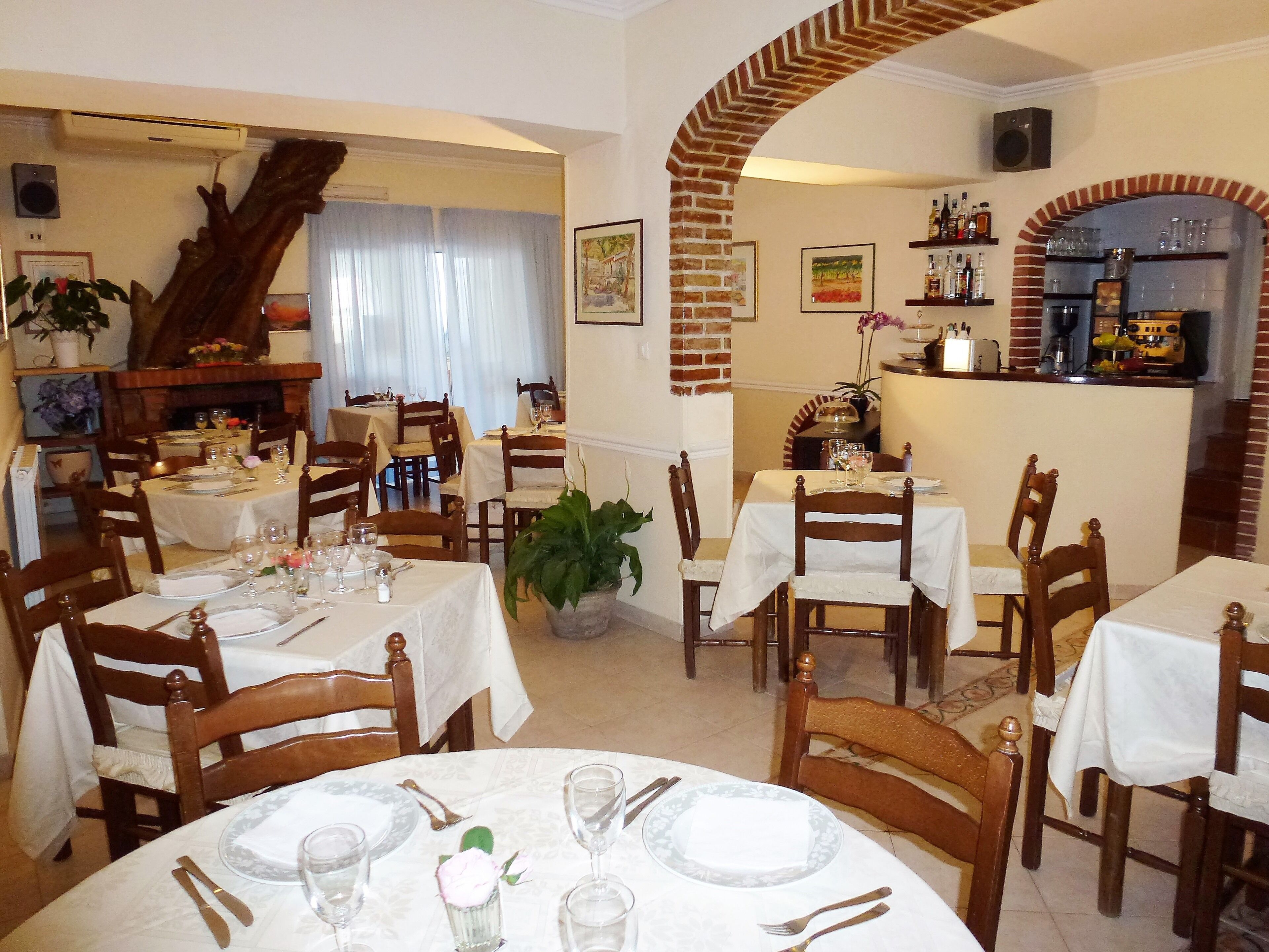 Un restaurante con varias mesas preparadas para comer, que presenta un arco de ladrillo y una zona de bar con estantes llenos de botellas y copas.