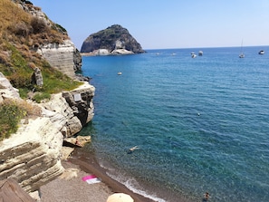 A coastal scene with a rocky cliff, clear blue sea, and boats.
