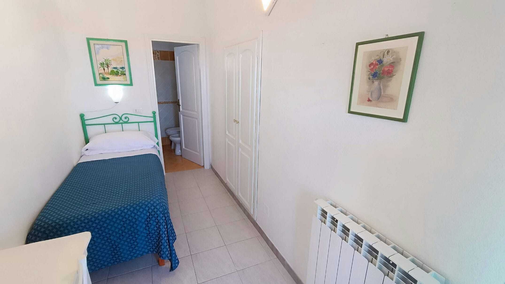 A small, narrow room with a single bed, a white radiator, and a door leading to another room.