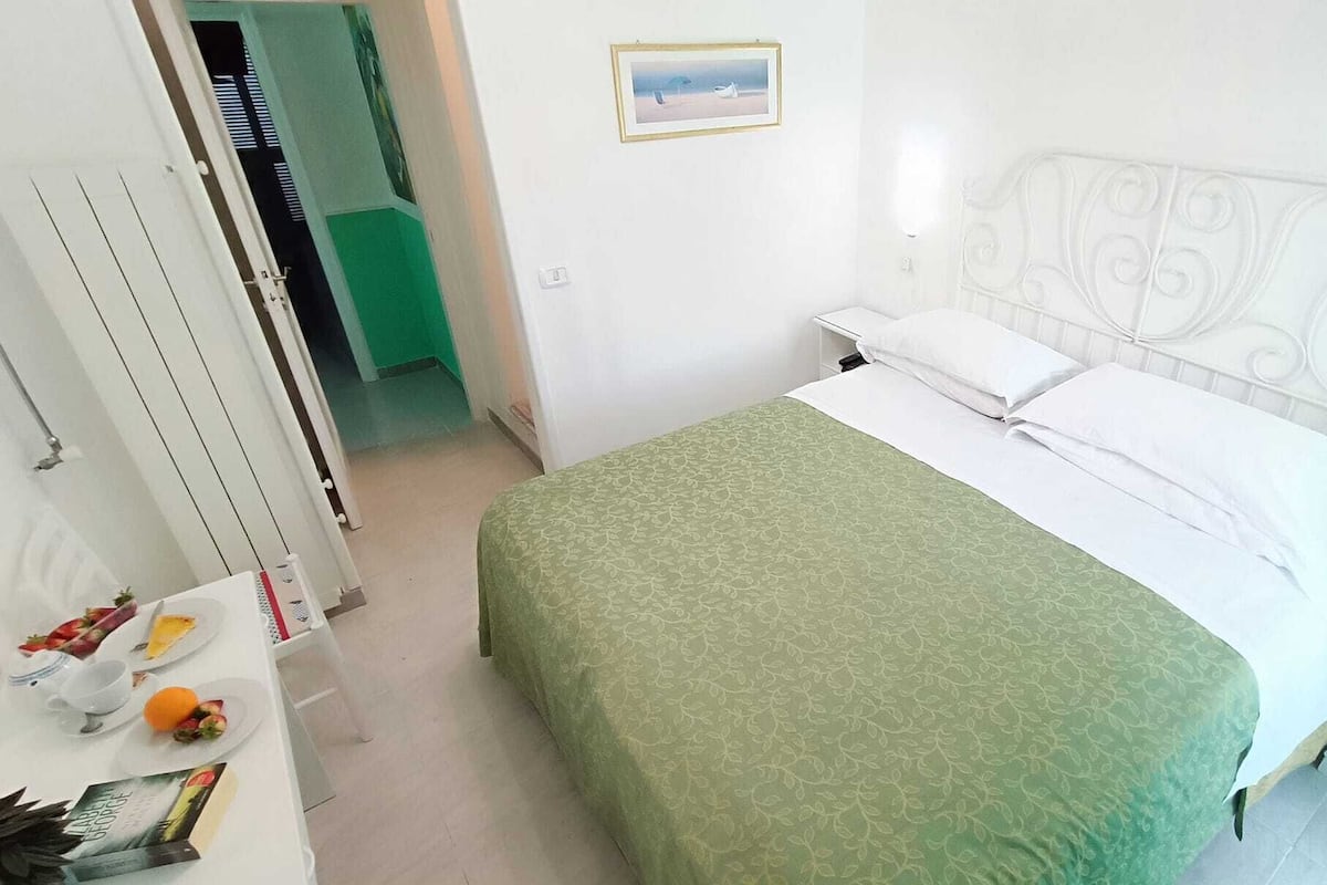 Een slaapkamer met een bed, nachtkastje, dressoir en een deur naar een andere kamer.