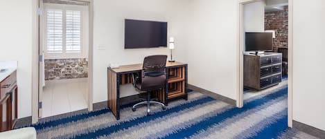 A room with a desk, chair, TV, and a brick wall.