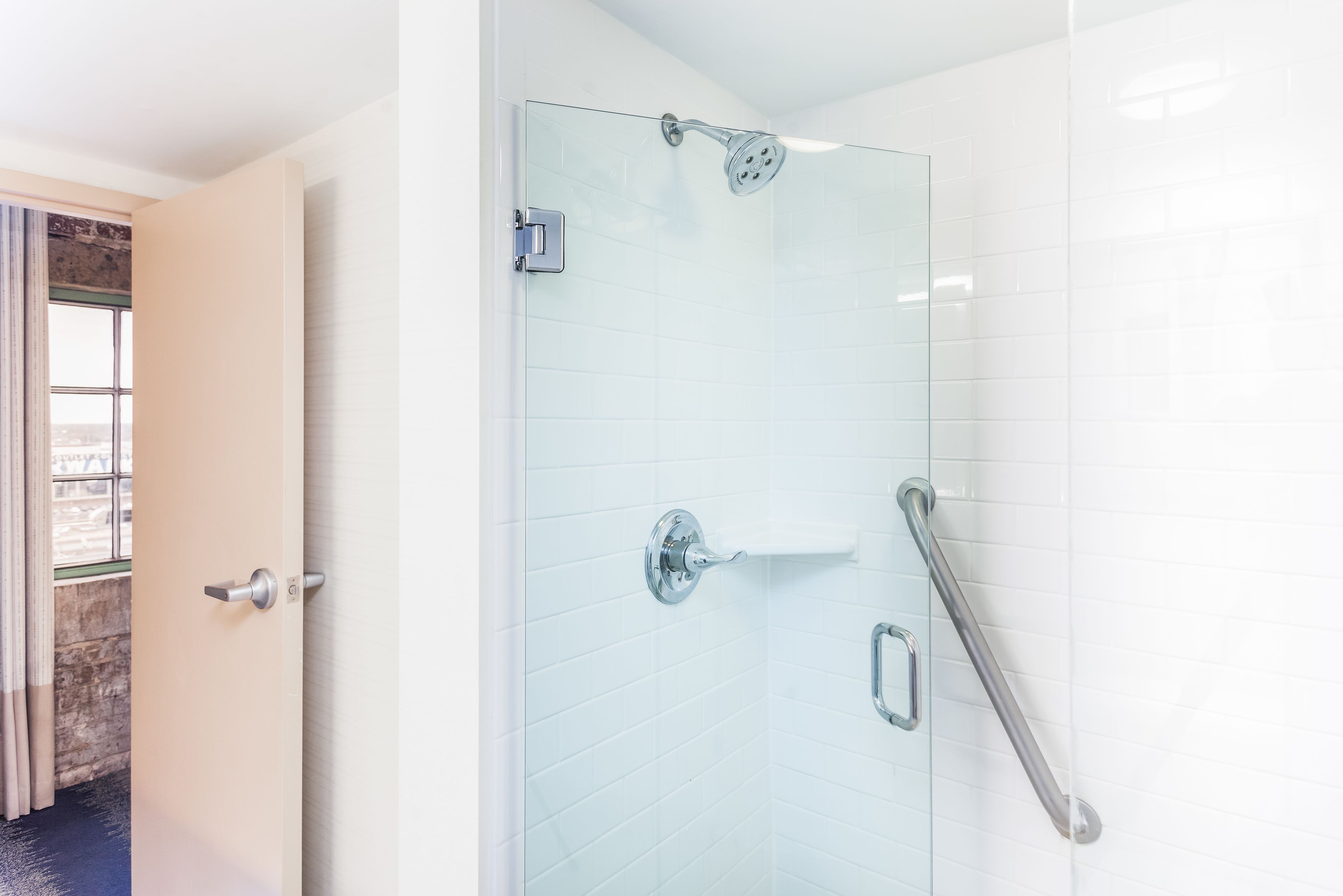 Une paroi de douche en verre avec un pommeau de douche à main, une barre à serviettes et une barre d’appui.
