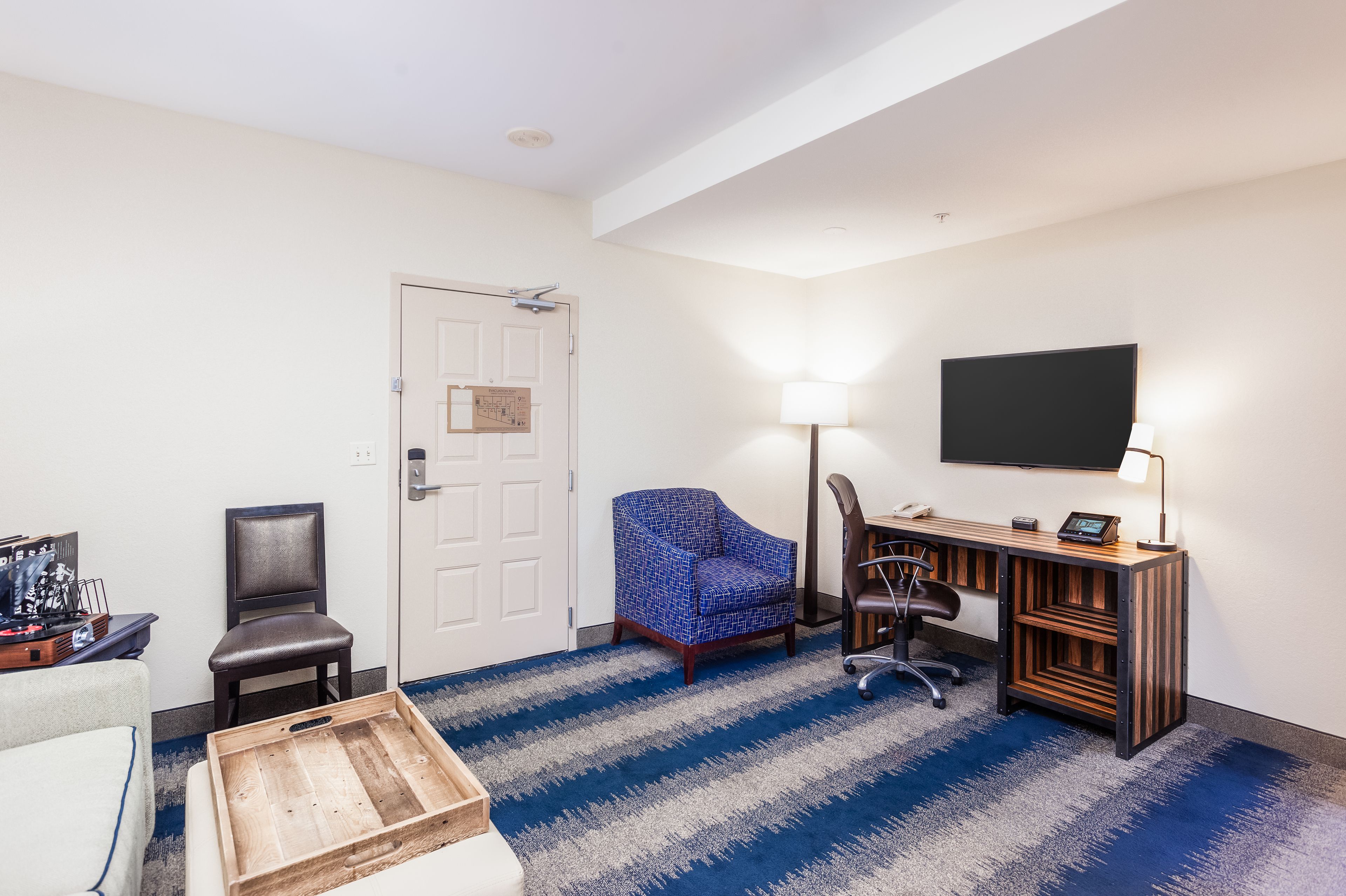 A hotel room with a desk, chair, TV, and a blue striped carpet.