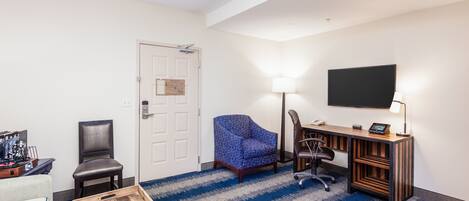 A hotel room with a desk, chair, TV, and a blue striped carpet.