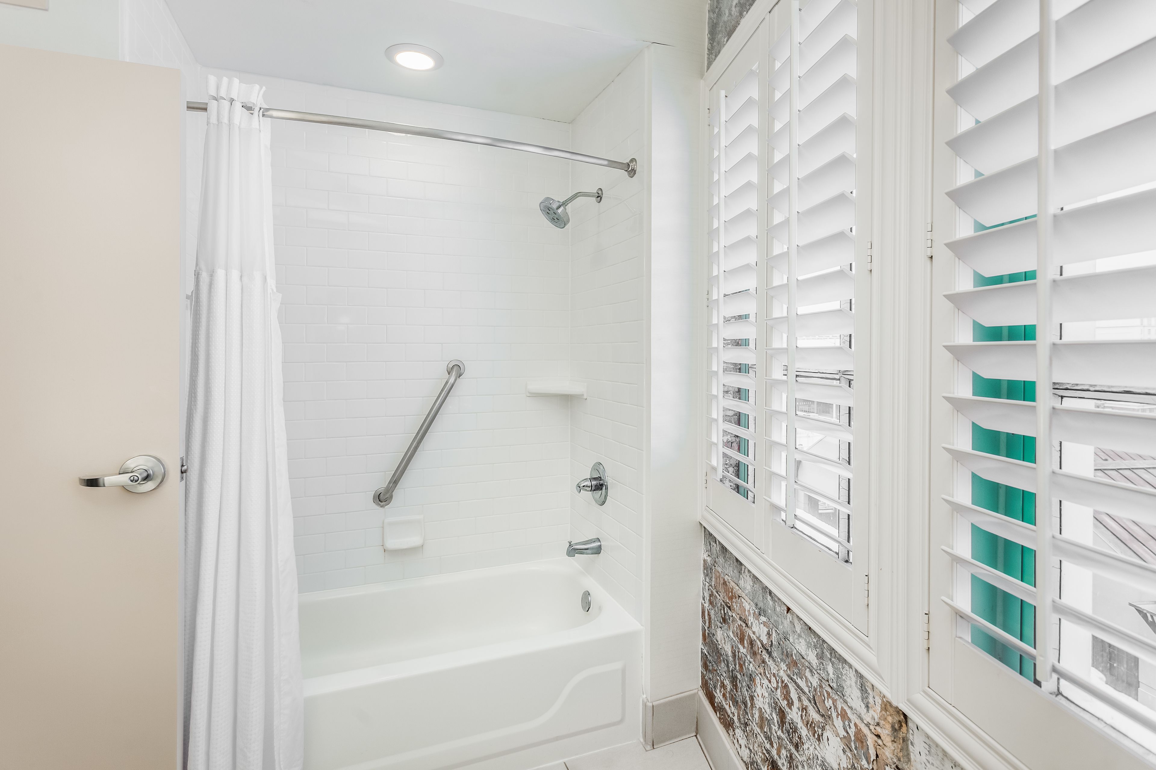 A modern bathroom with a white bathtub, a shower area, and a window with white shutters.