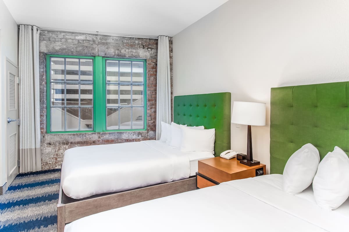 Habitació d'hotel amb un llit doble, un capçal de llit verd, una tauleta de nit amb una làmpada i una finestra amb emmarcadura verda.