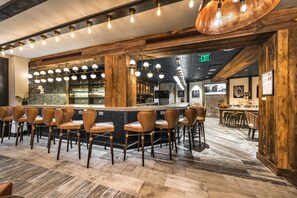 Un espace bar avec des chaises en bois et un comptoir, agrémenté d’un mélange de luminaires suspendus et de suspensions.