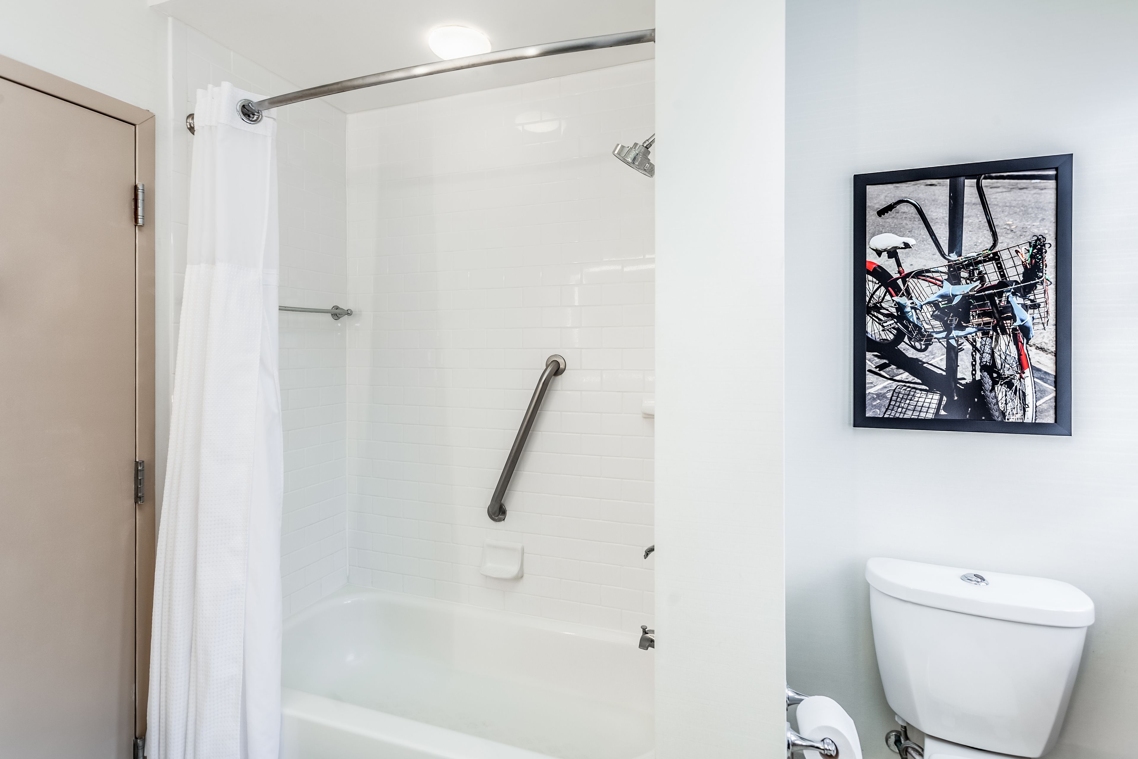 A modern bathroom with a glass-enclosed shower, a white toilet, and a framed abstract art piece on the wall.