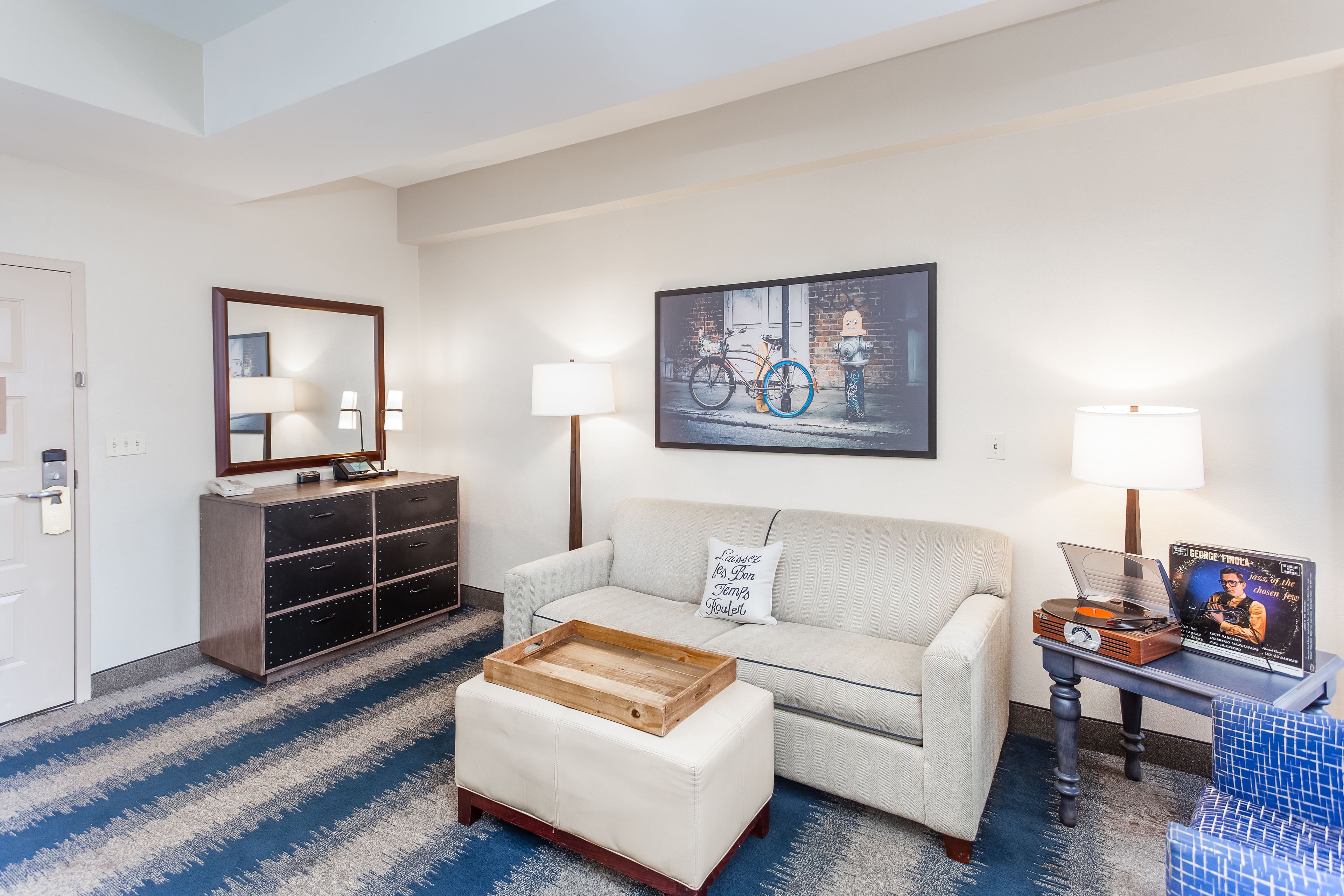 A modern living room with a sofa, a coffee table, a side table with a lamp, a dresser, and a wall-mounted TV.